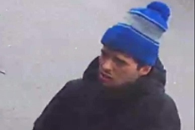 A man is pictured wearing a blue winter hat, a dark jacket and blue jeans.