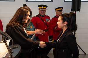 Teenage girl shakes the hand of a female judge, with RCMP officers in red serge in the background.