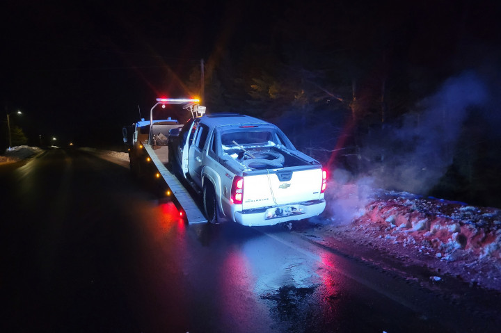 A Chevrolet Avalanche is pulled onto the flatbed of a tow truck, on the side of a road. 