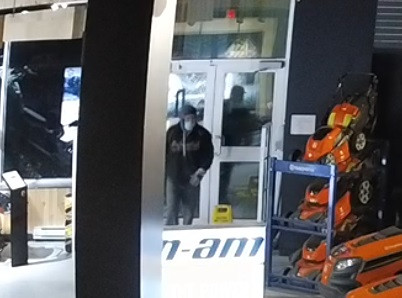 Un individu masqué à l'intérieur d'un commerce, portant des gants et un chandail à capuchon foncé.