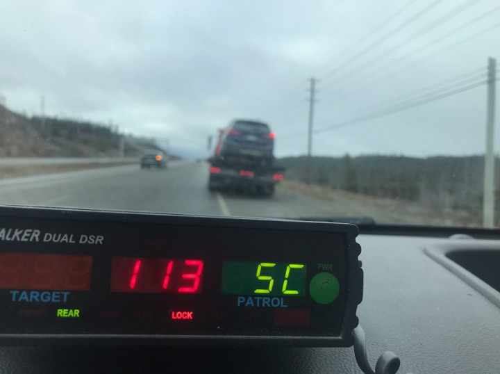 Un radar sur le tableau de bord d'un véhicule de police affiche une vitesse de 113 km/h. Un véhicule sur le plateau d'une dépanneuse en bordure de route.