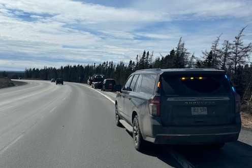 An unmarked police vehicle is stopped on the side of the highway. Pictured in front of the police vehicle is a tow truck and two other vehicles, parked on the side of the highway.