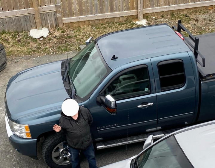 A photo of a man, with his face hidden, standing in front of a blue Chevrolet Silverado truck. 