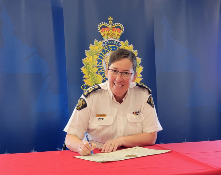 A/Commr Jennifer Ebert sits at a table with a red tablecloth signing the RCMP Renewed Core Values Document. 