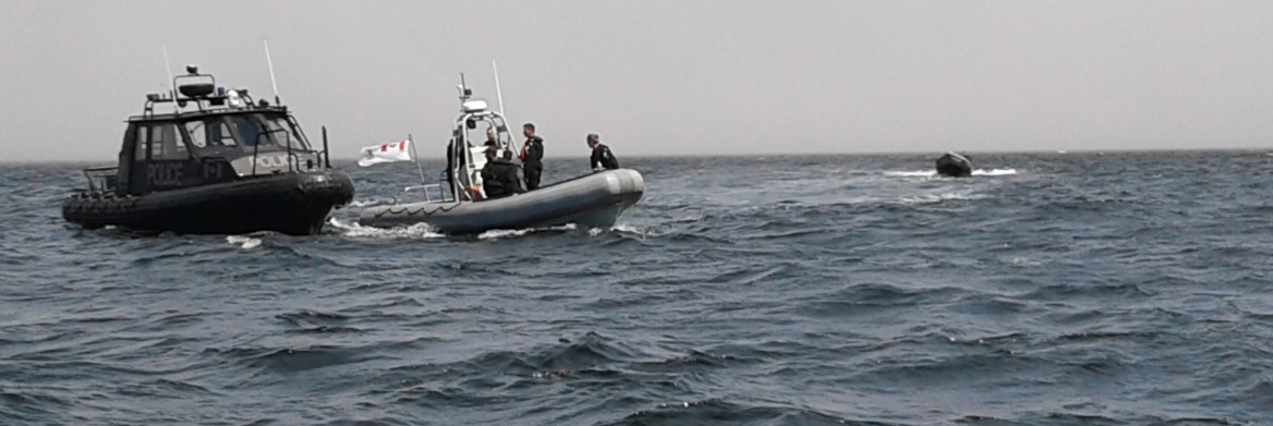 Three police officers on a boat next to another boat in the ocean.