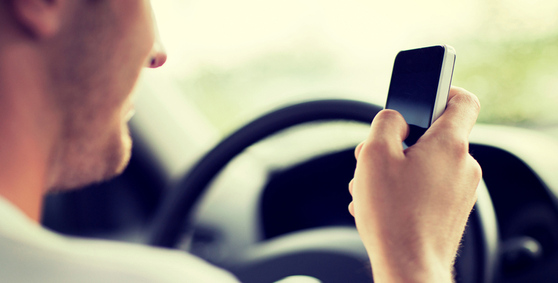 Un homme utilise son cellulaire tout en conduisant.