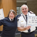 The RCMP Commissioner Brenda Lucki stands beside Assistant Commissioner Ches Parsons each holding a sign that reads 