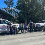 A group of school children colourfully drawing on two police vehicles using dry erase markers as part of the Colouring a Police Vehicle event as community RCMP officers and teachers supervise them.