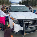 A group of school children from Kwanlin Dün First Nation drawing on a police vehicle using dry erase markers as part of the Colouring a Police Vehicle event.