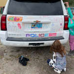 Two small children colourfully drawing on a police vehicle using dry erase markers as part of the Colouring a Police Vehicle event.