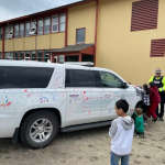 Two small children drawing on a police vehicle using dry erase markers as a police officer watches as part of the Colouring a Police Vehicle event