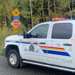Colourfully marked RCMP police vehicle parked on the side of the road near a school zone sign after being drawn on by children during the Colour the Cruiser event.