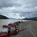 Multiple canoes coming to shore along a stretch of the river