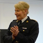A female RCMP officer speaks to a room of new cadets in civilian clothing.