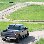 A pickup truck prepares to drive down a dirt hill into a flooded road.