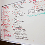 A white board in a kitchen with the day’s menu written out.