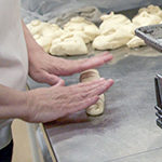 A baker rolls out dough, placing it on a sheet-pan.