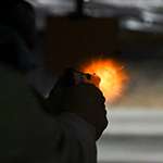 A cadet fires their pistol at a target on a dark shooting range. 