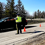 A cadet directs traffic on a summer day. There are bright orange pylons and the cadet wears a high visibility vest. 