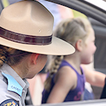 A cadet wearing a Stetson hat shows a little girl how to use the lights in a police car.