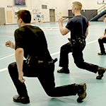 Cadets do walking lunges in a gym.