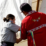 A Knowledge Keeper demonstrates how to set up a tipi with a cadet. 