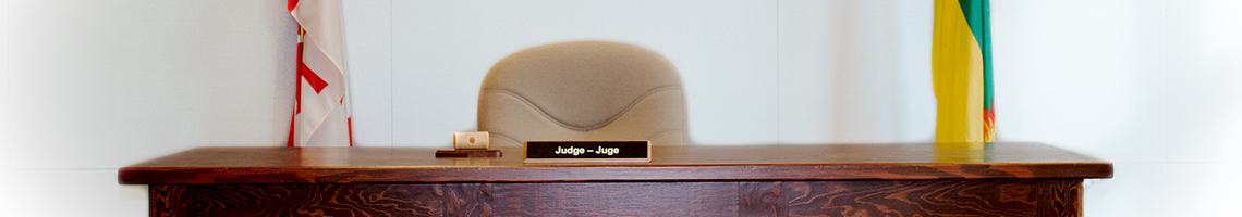 A wooden desk with a sign that says judge. There is a Canada and Saskatchewan flag behind. 