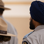 Cadets stand together looking forward. Some cadets are wearing Stetson hats and one wears a navy turban. 
