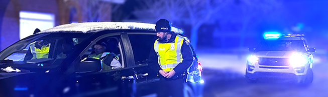 A cadet speaks to the driver of a vehicle at night.