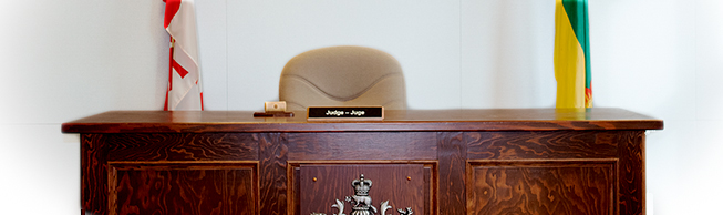 A wooden desk with a sign that says judge. There is a Canada and Saskatchewan flag behind. 