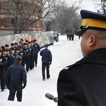 A Drill corporal watches a troop march in the snow.
