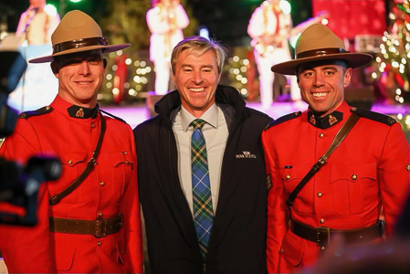Two male RCMP officers in red serge are standing on opposite sides of Tim Houston, the premier of Nova Scotia.