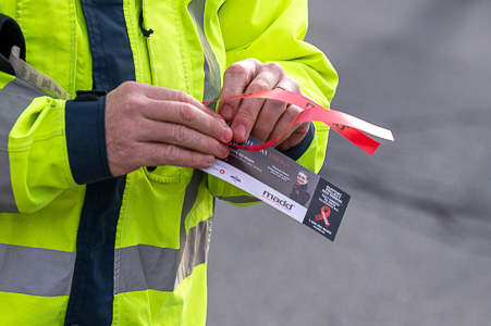Two hands, pictured close up, are holding a red ribbon and a MADD Canada brochure.