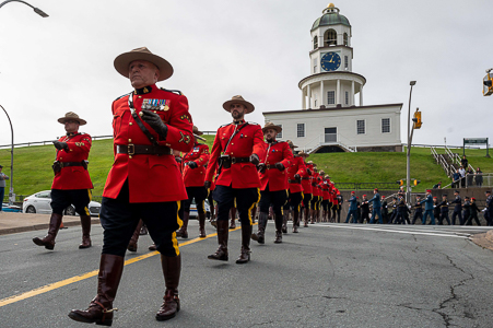 Several RCMP members in red serge are marching along a downtown Halifax road. The town clock, and members of another police service, are in the background.