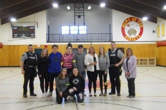 Group photo including two RCMP officers, volunteers and youth in gym of youth centre.