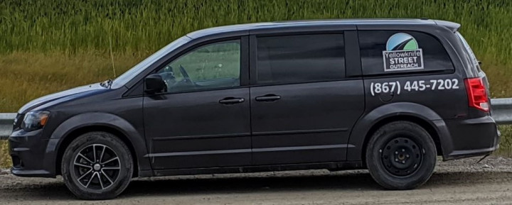 A dark minivan parked in front of long grass