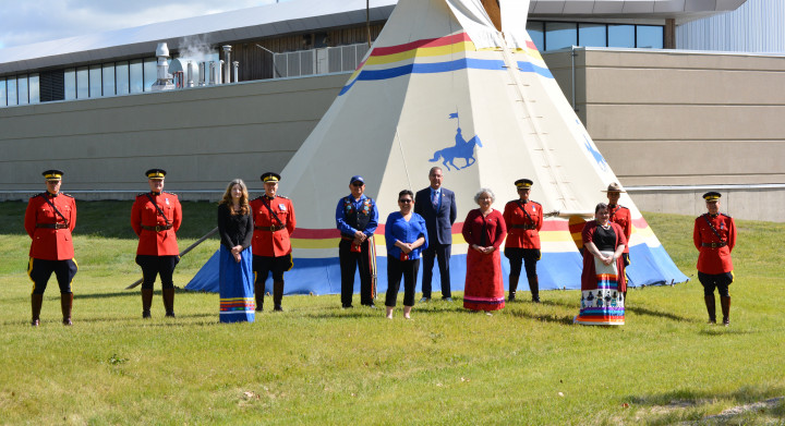 Saskatchewan RCMP officers dressed in Red Serge stand facing the camera in rows alongside ceremony witnesses and guests outside of the tipi
