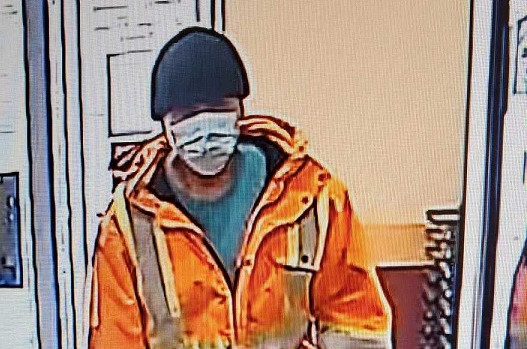 An individual wearing an orange coat with reflective stripes, a black hat, a disposable face mask and jeans enters the Newfoundland and Labrador Liquor Corporation.