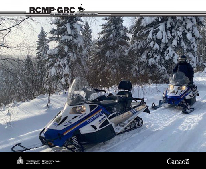 Un officier est assis sur une motoneige ; il y a une deuxième motoneige au premier plan et des arbres et de la neige en arrière-plan.