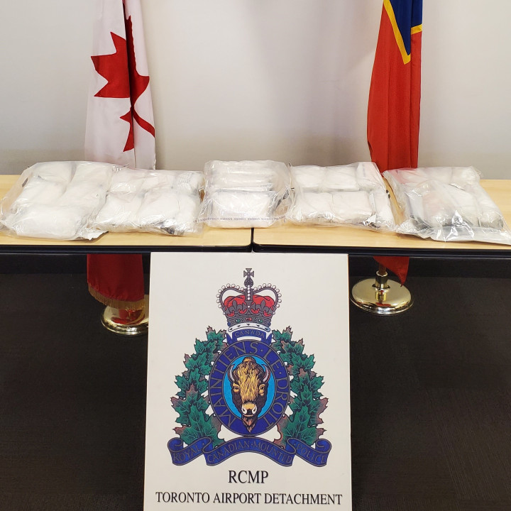 28 kg of ketamine that was seized as part of the RCMP Toronto Airport Detachment investigation. The ketamine packages are displayed on a table with an RCMP Toronto Airport Detachment sign and the Canadian and O Division ensign flags in the background. 