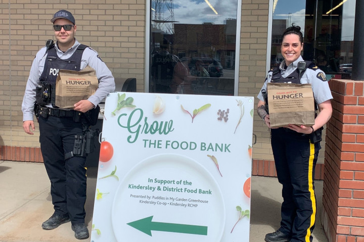 two RCMP officers standing and one officer sitting with food donations in support of the Kindersley & District Food Bank filling the truck box