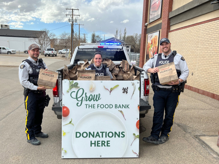 three RCMP officers standing and one officer sitting with food donations in support of the Kindersley & District Food Bank filling the truck box