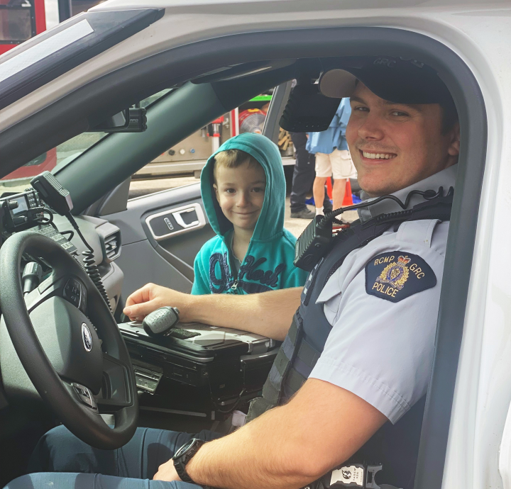 Policier assis dans une voiture de police à côté d'un enfant souriant.