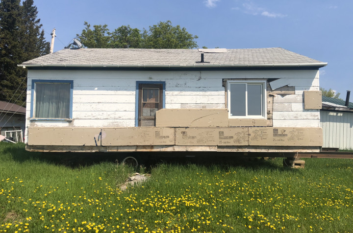 A small, white bungalow sits on top of a trailer