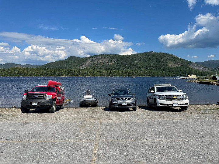 From left to right, a red Ford Bay of Islands Search and Rescue truck and a zodiac boat, a Transport Canada grey Nissan SUV and a marked RCMP Chevrolet Tahoe are parked at the shoreline of the ocean near Corner Brook.