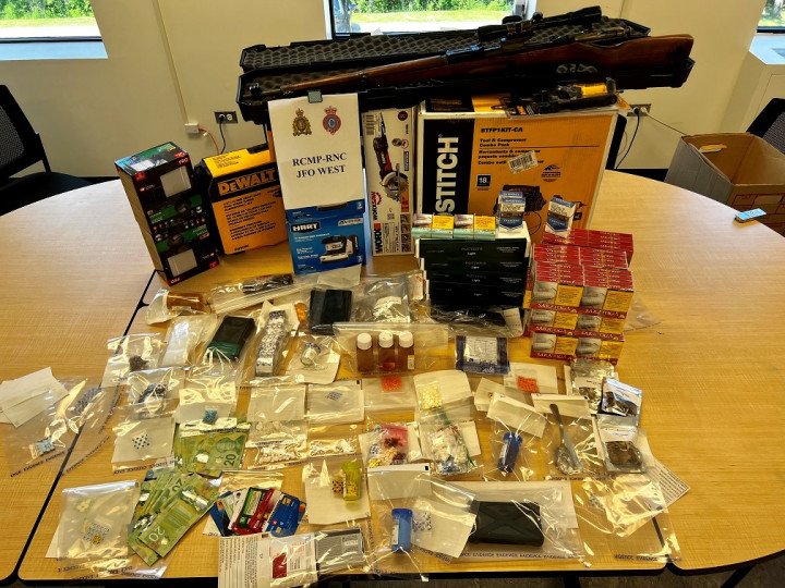 Various bagged items of drugs and drug paraphernalia, a firearm, cash, contraband packages of cigarettes and stolen tools are set out on a table on display with a sign that says RCMP-RNC JFO West.