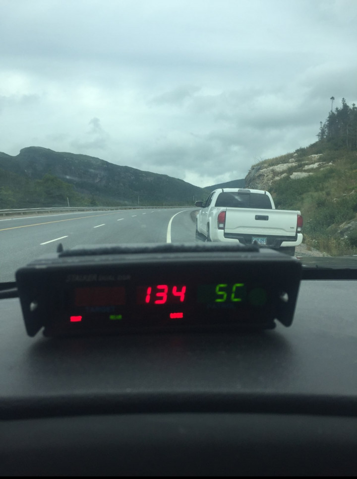 Le radar d'une voiture de patrouille indique une vitesse de 134 km/h, en rouge. Par le pare-brise, on voit la route sous un ciel couvert et une camionnette blanche rangée sur le côté.