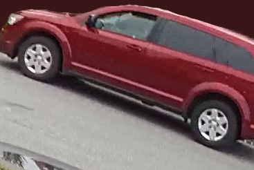 Un SUV Dodge Journey rouge roule sur une route asphaltée. L'arrière-plan a été noirci.
