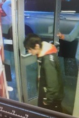 A male is entering a convenience store. He is wearing a black Helly Hansen jacket, black pants and a yellow and red hoodie. He has dark colored hair.