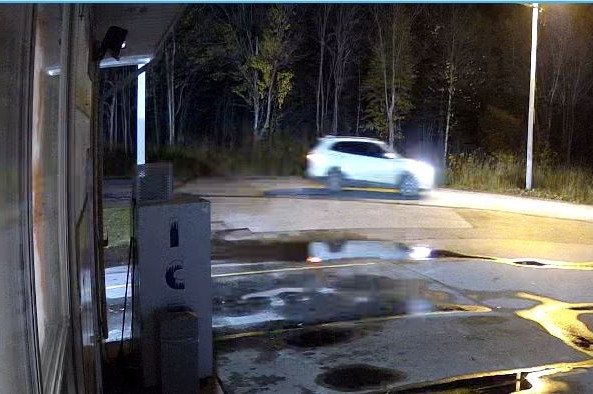 A white SUV with tinted windows is captured on video surveillance driving past a gas station at night during the time of a break and enter.